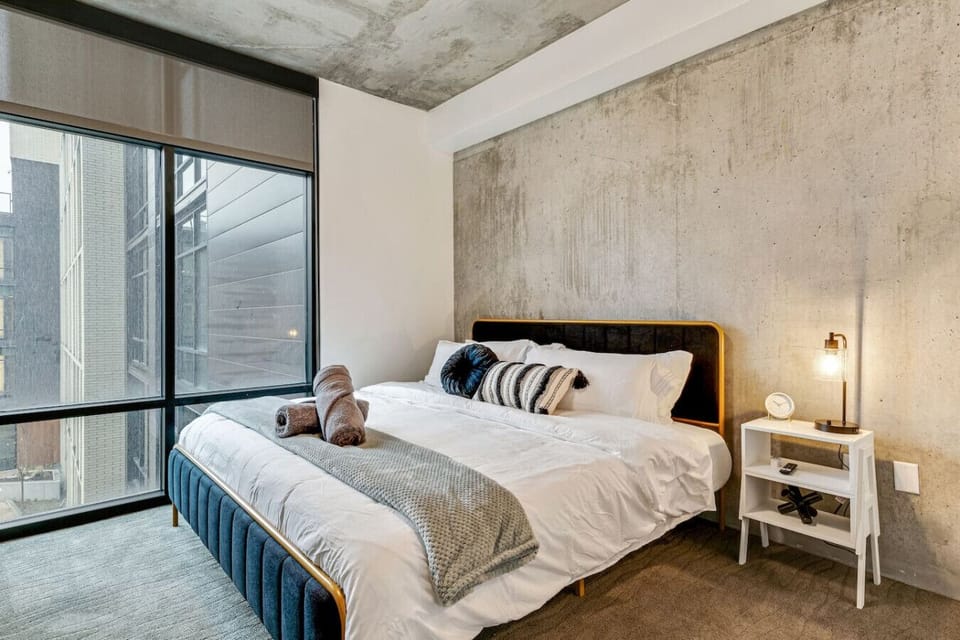 Cozy bedroom with industrial charm, soft bedding, and floor-to-ceiling windows filling the space with natural light 🌆🛏️✨