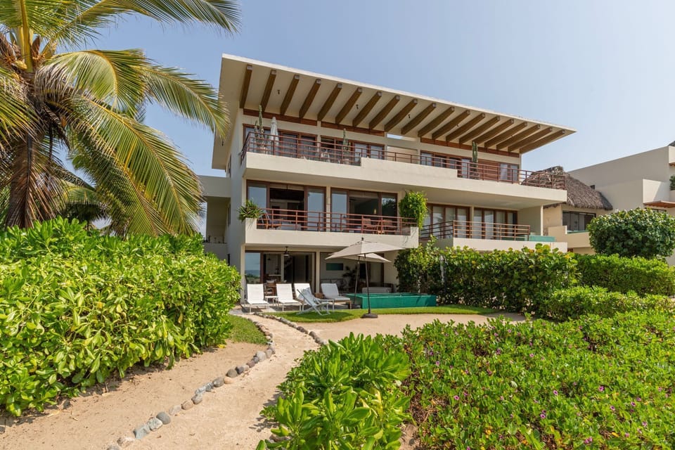 A stunning three-story beachfront villa surrounded by lush landscaping, offering a peaceful retreat.