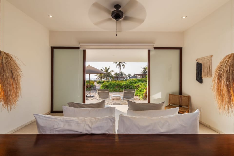 Wake up to the sound of waves in this tranquil bedroom featuring floor-to-ceiling windows, natural decor, and direct access to a private terrace.