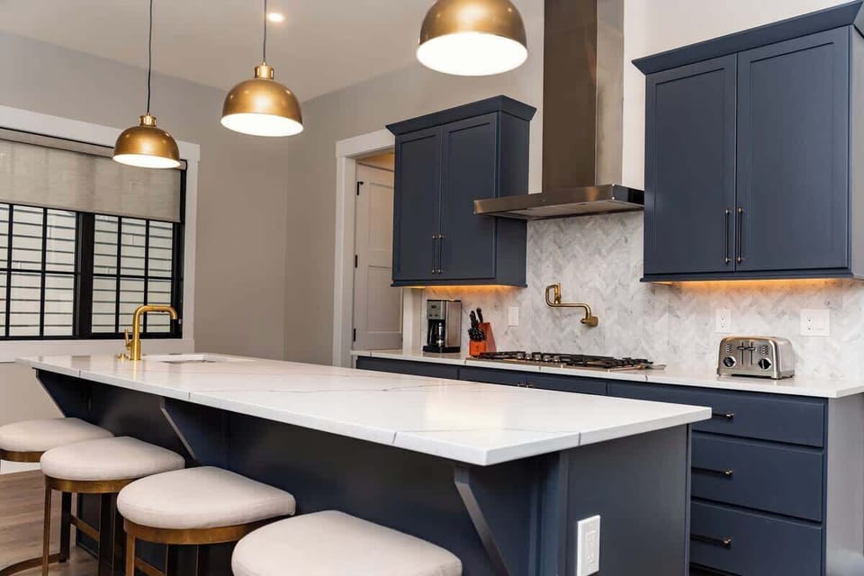 - Sleek kitchen with navy cabinets marble backsplash and gold fixtures
- Spacious island with bar seating provides room for casual dining
- Pendant lights create a warm and inviting cooking space