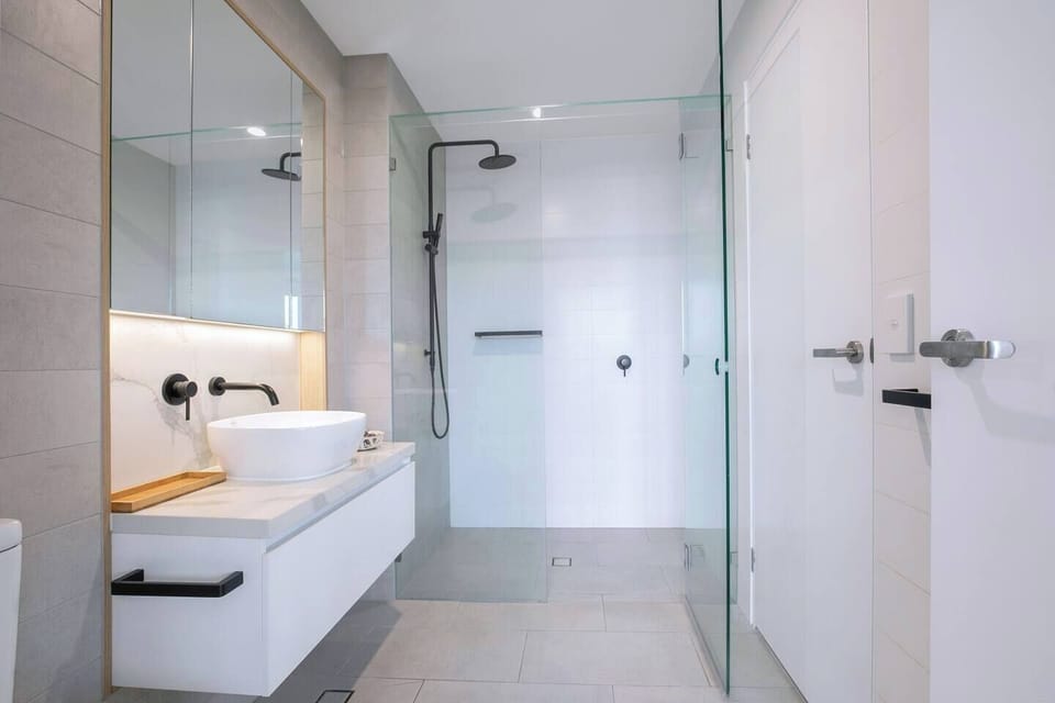 The stylish, contemporary bathroom is immaculately appointed with a rain shower, modern vanity and mirror. 
