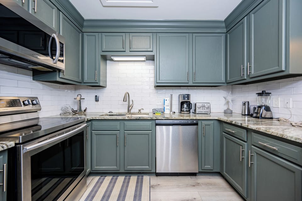 Modern kitchen features sleek green cabinetry, granite countertops, and essential appliances, perfect for vacation meal prep