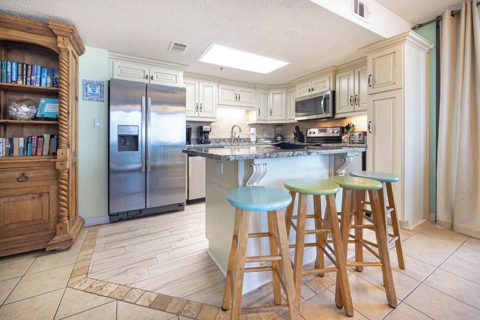 Kitchen area features a granite countertop, stainless appliances, and a breakfast bar with colorful stools for casual dining
