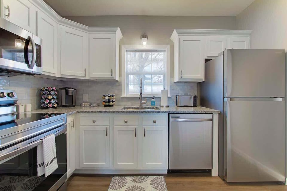 Fully equipped kitchen w/ stainless appliances, white cabinetry & bright window over the sink