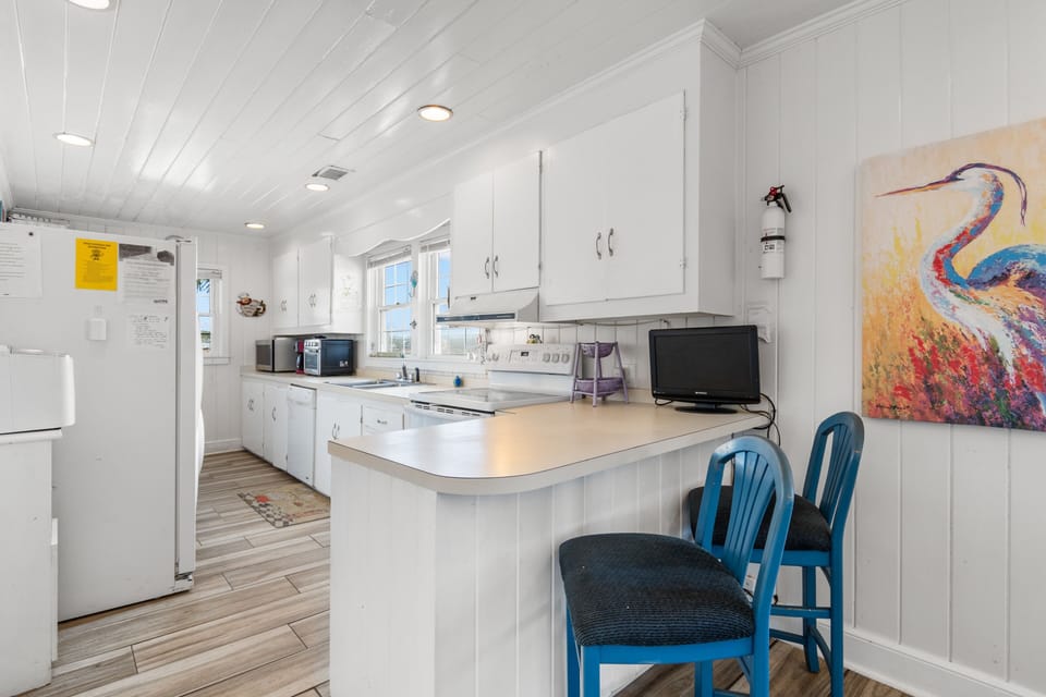 Your bright white kitchen features modern appliances and a breakfast bar where you can enjoy morning coffee with colorful local artwork.