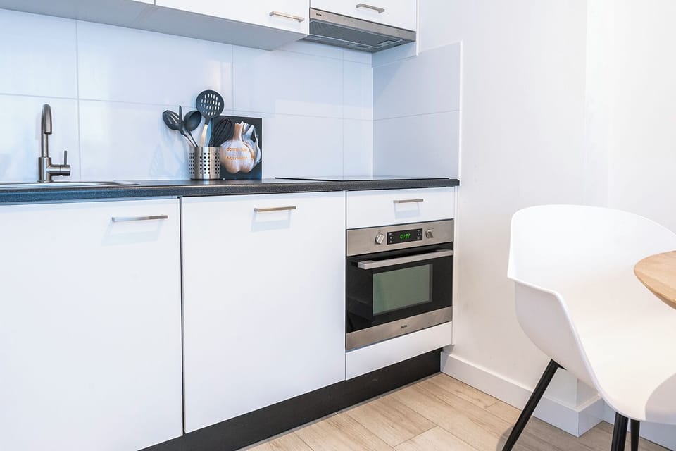 Minimalist cooking space with essential utensils in a metallic holder, a black ceramic cooktop, and an elegant cookbook, all complemented by a crisp white tile backdrop.