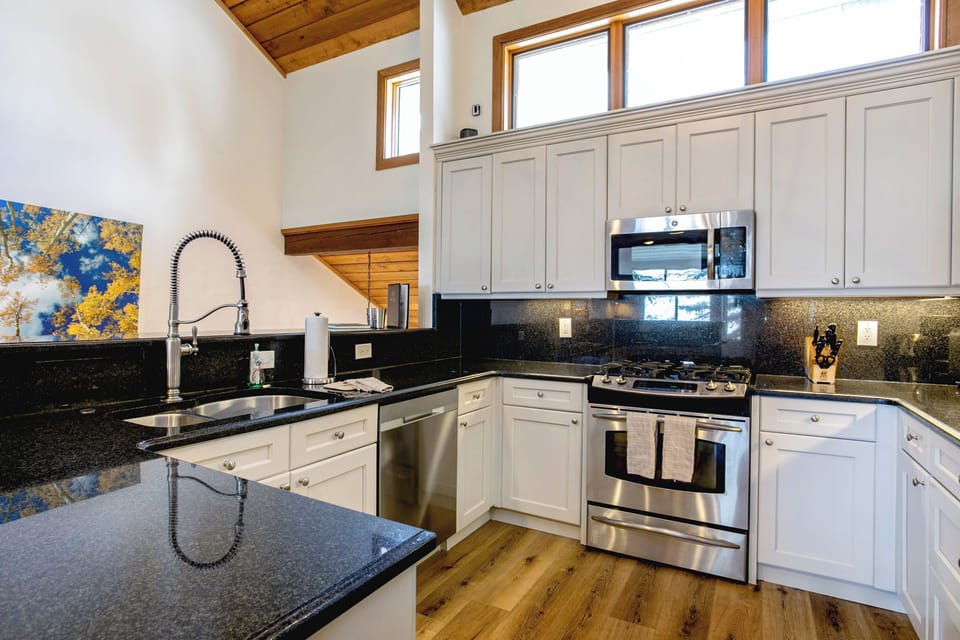 A modern kitchen with white cabinets, stainless steel appliances, a black granite countertop, and a mounted painting on the wall.