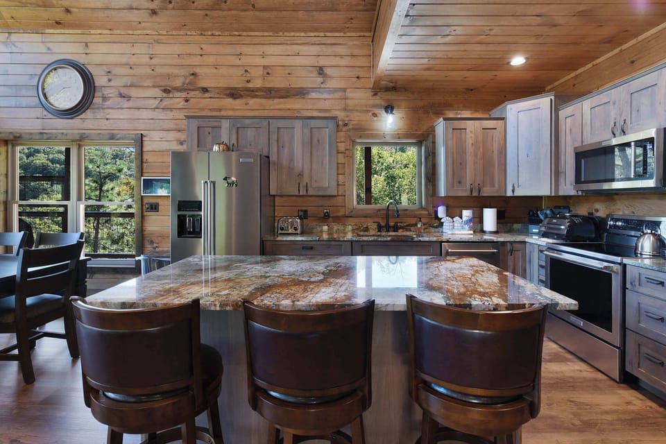 rustic kitchen with granite island and stainless steel appliances overlooking forest views