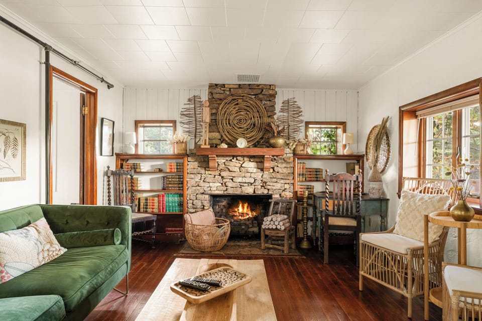 - Relax in a stylish living room with a stunning stone fireplace
- Green velvet sofa and curated décor offer vintage charm
- Shelves of books, natural textures, and cozy lighting throughout