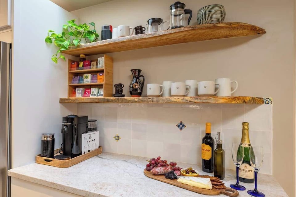 The coffee/tea station with a Nespresso machine, a selection of tea bags, a teapot, a French press, and a coffee grinder (drip coffee machine stored in a cabinet).