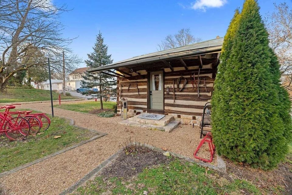 A side view shows the cabin's covered porch, landscaped grounds, gravel paths, and red cruiser bicycles.