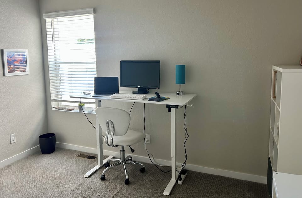 Bright office with adjustable stand up, sit down desk, monitor, shelves