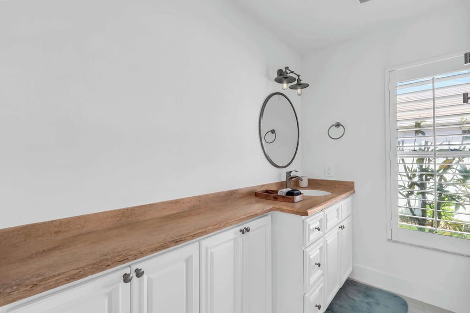 The second full sized bathroom has a long counter and a sink, mirror and plantation shutters on the window
