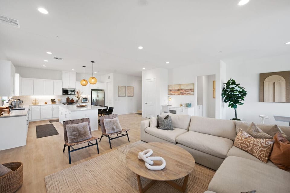 Open-concept living & dining area w/ cozy seating, warm wood accents & a bright kitchen backdrop.