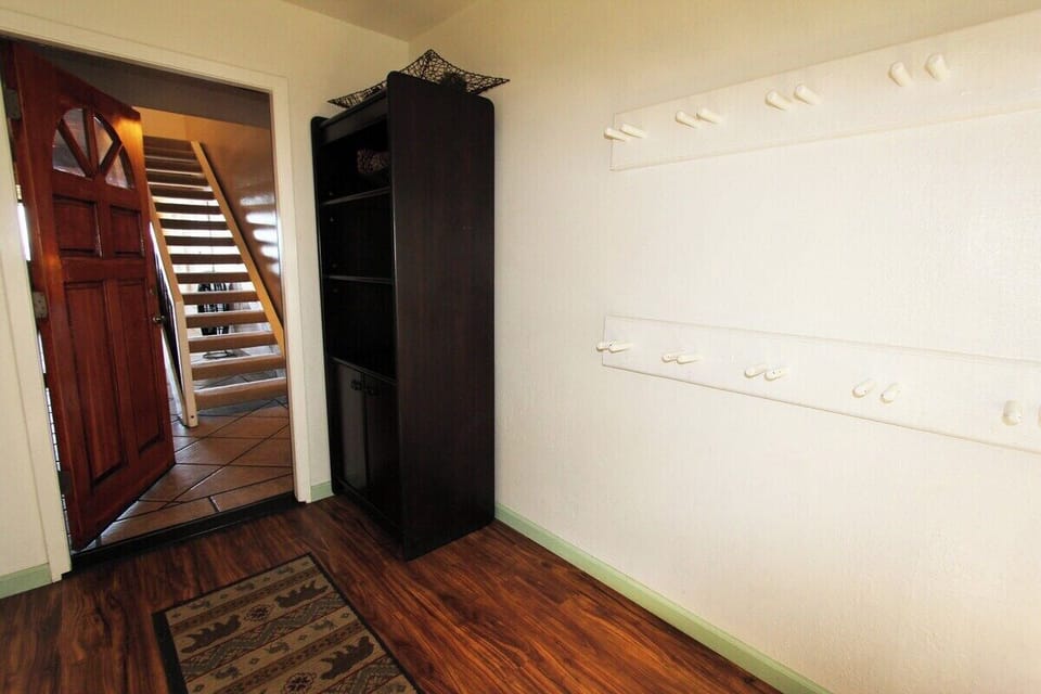 Entry area with wall hooks, shelving cabinet, rug, door, and staircase.
