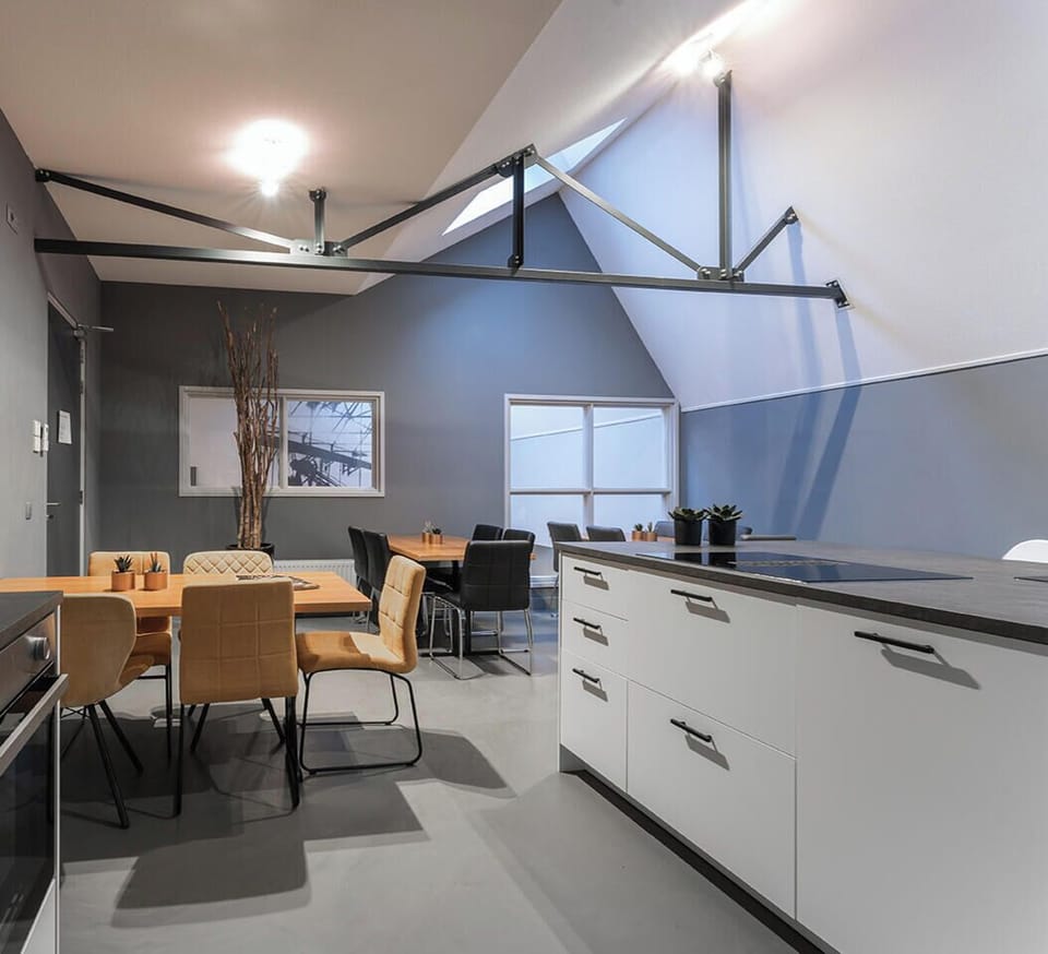 A spacious and modern kitchen under a striking angular ceiling with skylights, blending sleek white cabinetry and dark countertops for a contemporary look.