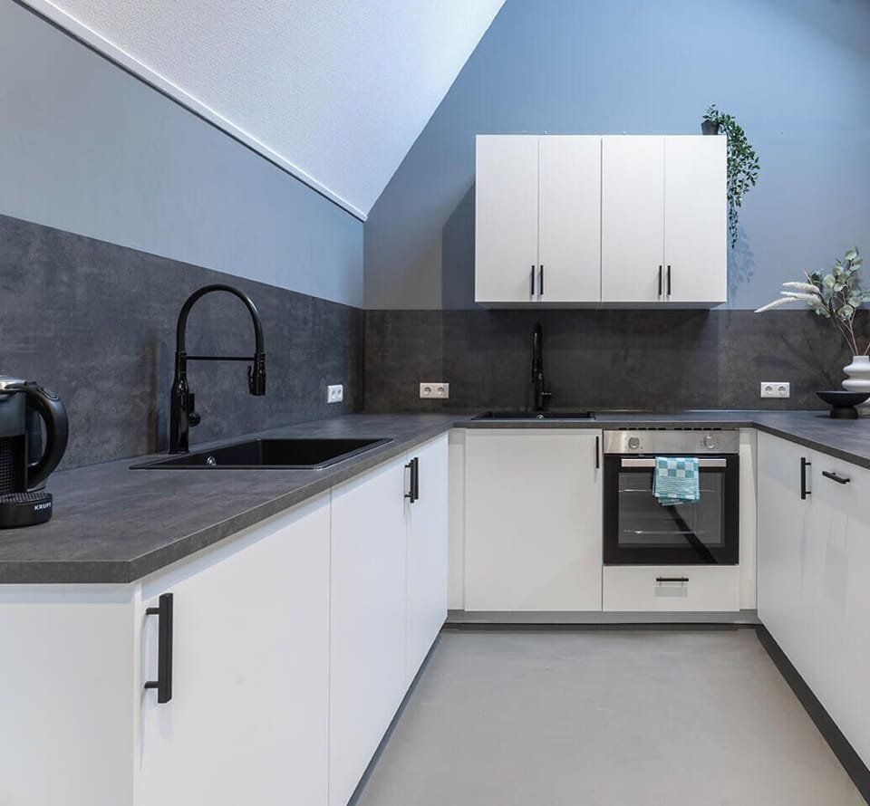 A spacious and modern kitchen under a striking angular ceiling with skylights, blending sleek white cabinetry and dark countertops for a contemporary look.