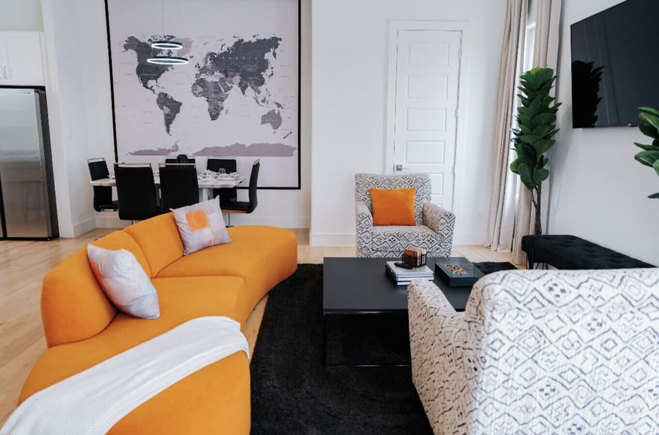 Sunlit living room with soaring ceilings, modern orange lounge seating, and an open-concept layout designed for comfort and connection.