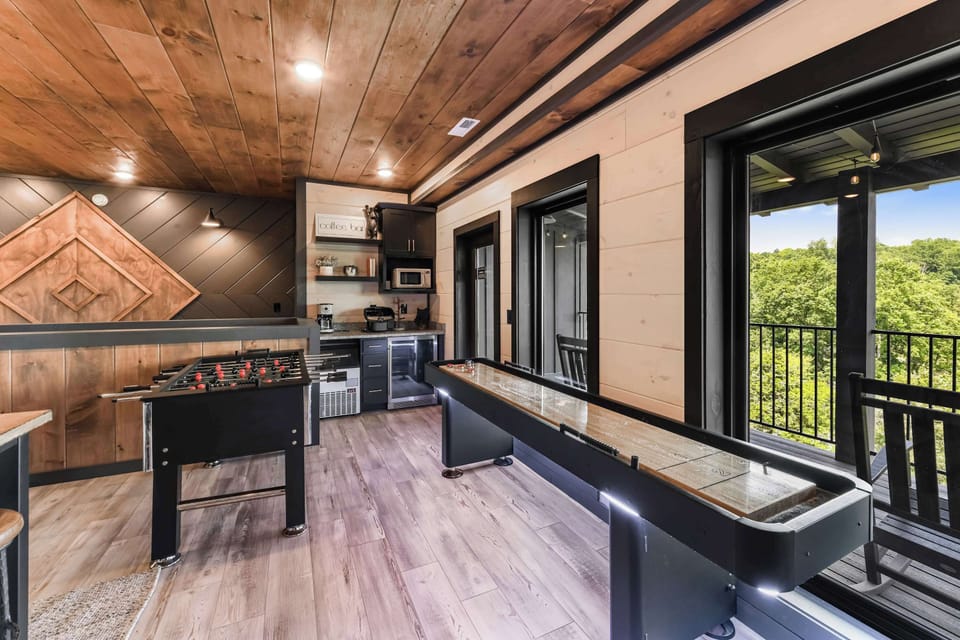 Game room with foosball, shuffleboard, and a coffee bar overlooking a forested view.