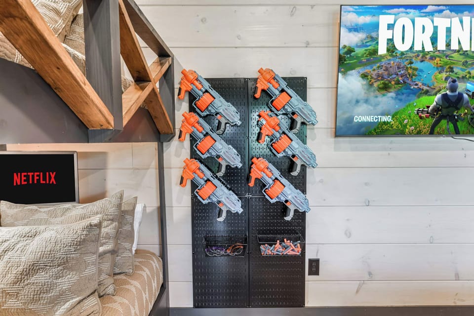 Game room corner with mounted toy blasters and a screen displaying a popular video game.