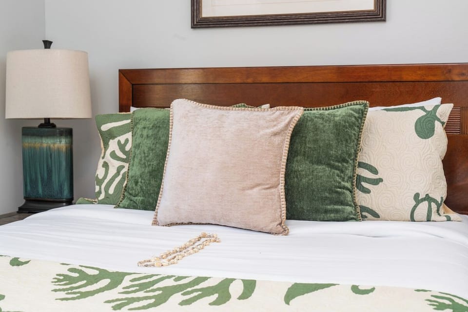 Close‑up of bed with decorative pillows, bedside lamp, and wooden headboard.