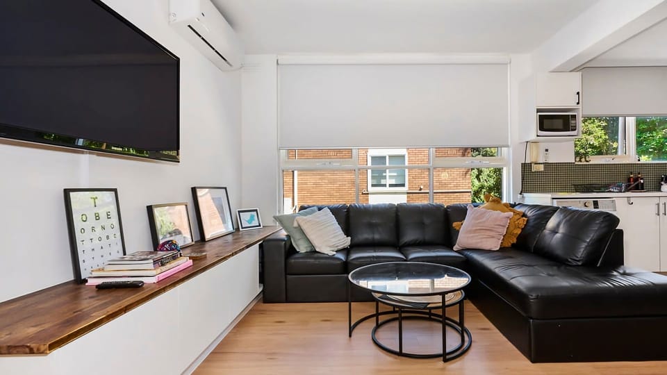 Enjoy movie nights with a sleek wall-mounted TV setup, a long floating media shelf for your favorite decor, and wide windows that invite plenty of natural light.