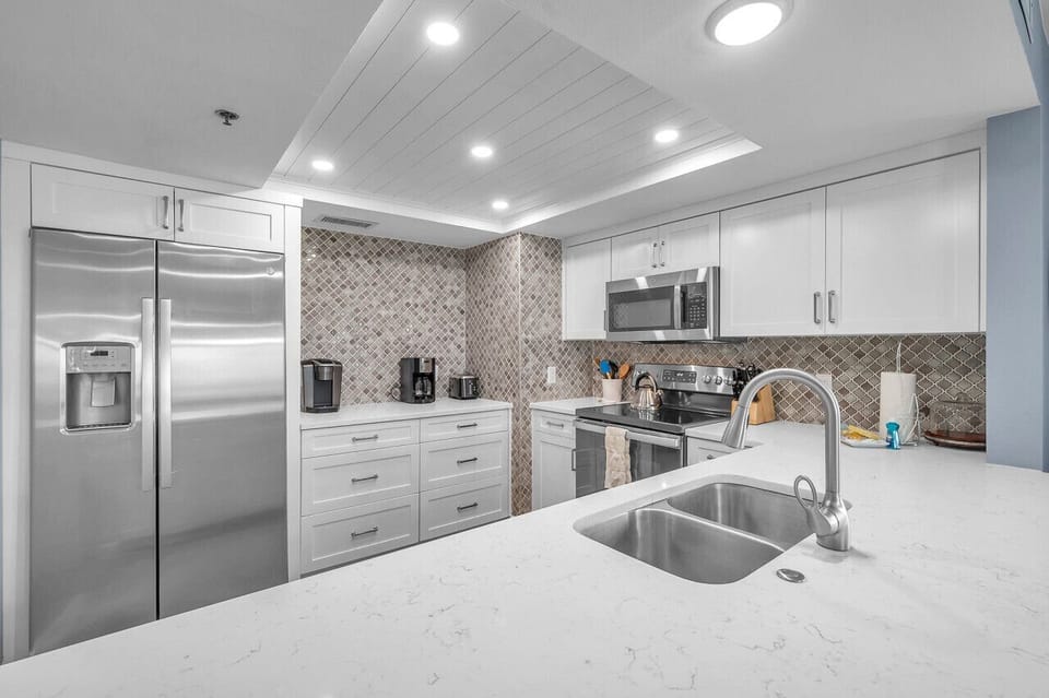 Modern kitchen view w/ stainless steel appliances, mosaic backsplash & ample prep space.