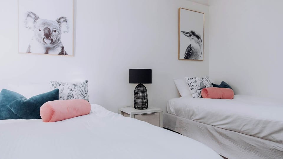 Playful Australian wildlife artwork and soft blush accents create a sweet, welcoming vibe in this bright twin-bed setup.