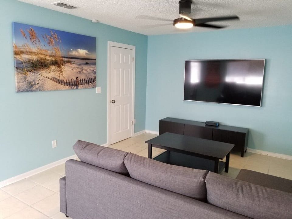 Bright living room with large TV, comfortable seating, and vibrant beach artwork.