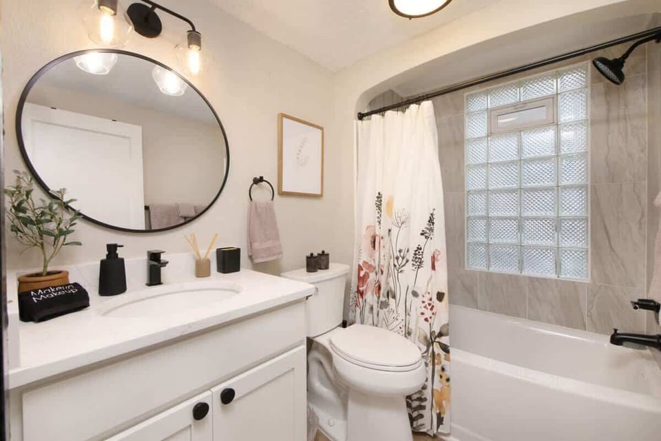 Full bathroom w/ double vanity, round mirror & shower-tub combo