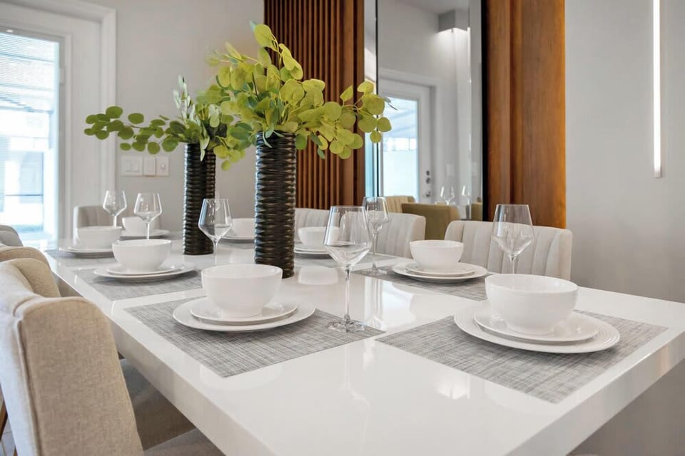 Modern dining table set for six with elegant glassware and fresh greenery.