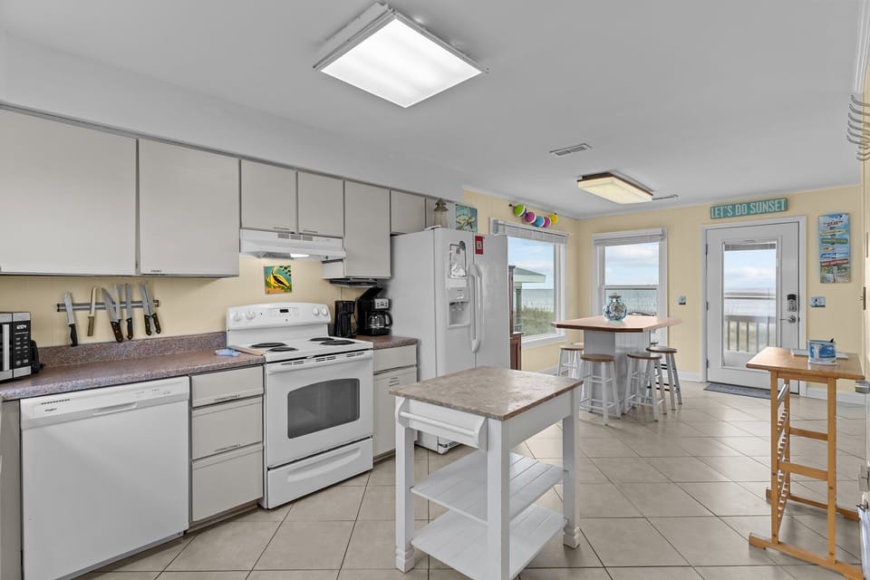 Oak Island, NC kitchen with white appliances, stove, sink, microwave, island cart, tile floors, beach décor, wood cabinet, and bright coastal style.