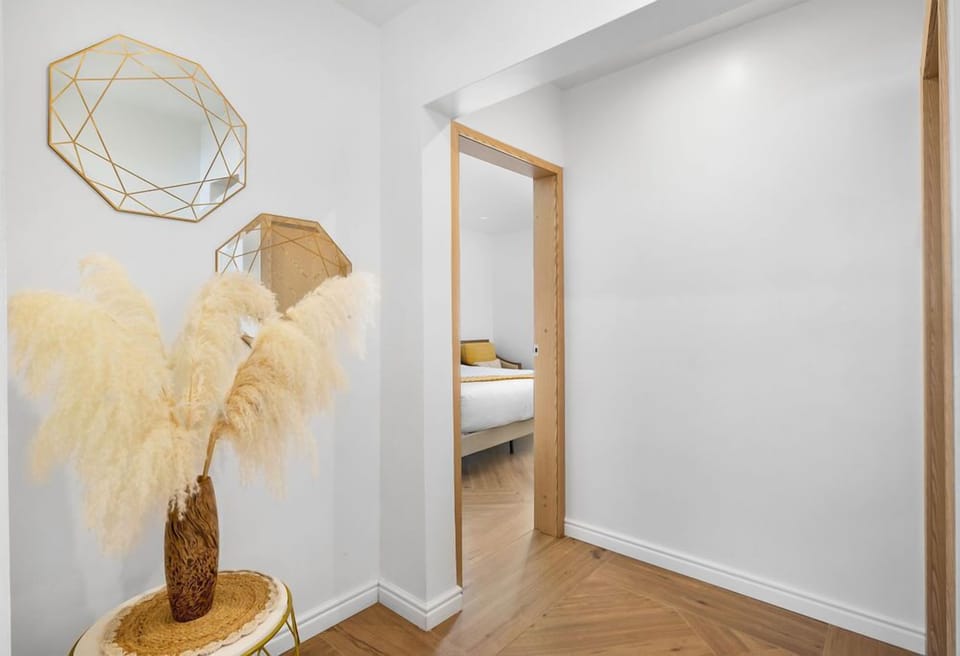 The space features crisp white walls and minimalist furnishings, with rich wooden accents and tropical plants adding a natural, earthy touch.