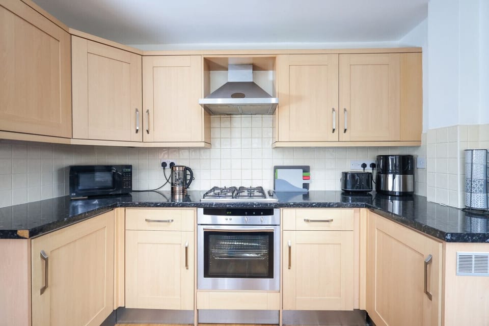 Functional kitchen with light cabinetry, dark countertops, and integrated appliances. Large windows provide natural light and lead to outdoor access. Includes sink, stove, and ample storage in an efficient layout.