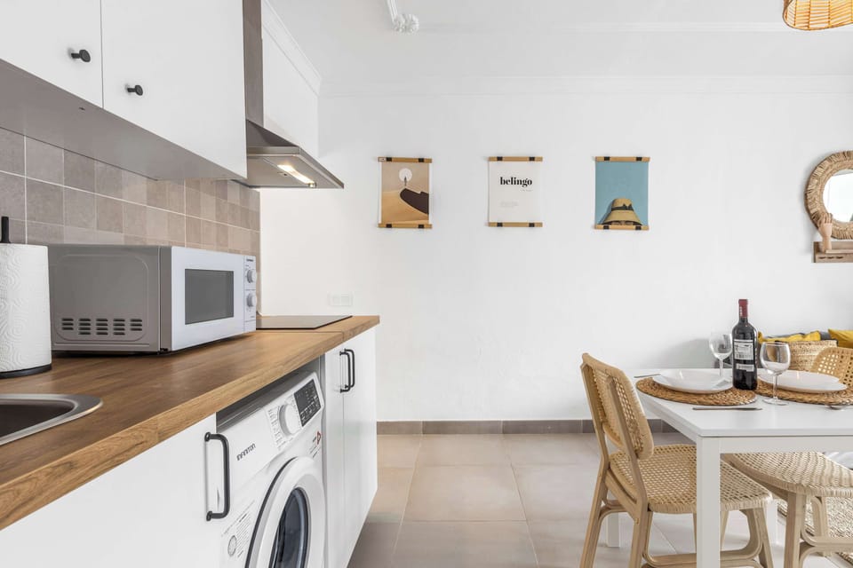 Cocina compacta y funcional con microondas, lavadora y detalles boho. 🍷🍽️ Ideal para preparar tus comidas con comodidad y estilo durante tu estancia.

