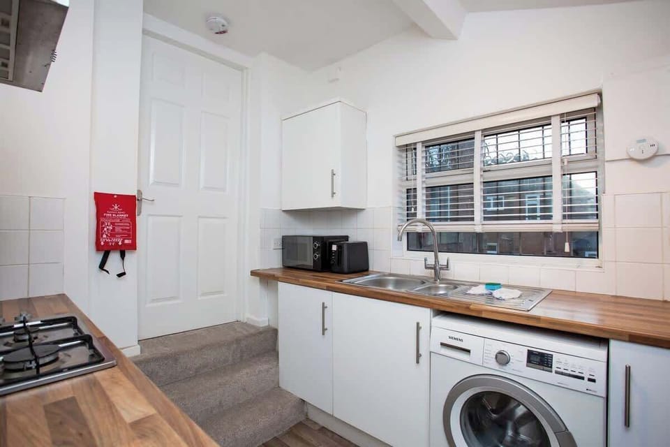Bright and modern kitchen with white cabinets, wooden countertops, a washing machine, and essential appliances. Compact and fully equipped.