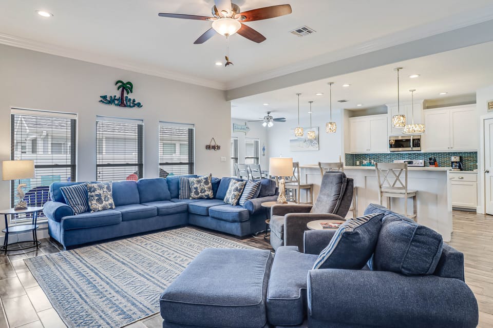 Relax in your spacious coastal-themed living room with plush blue sectionals and open kitchen beyond.