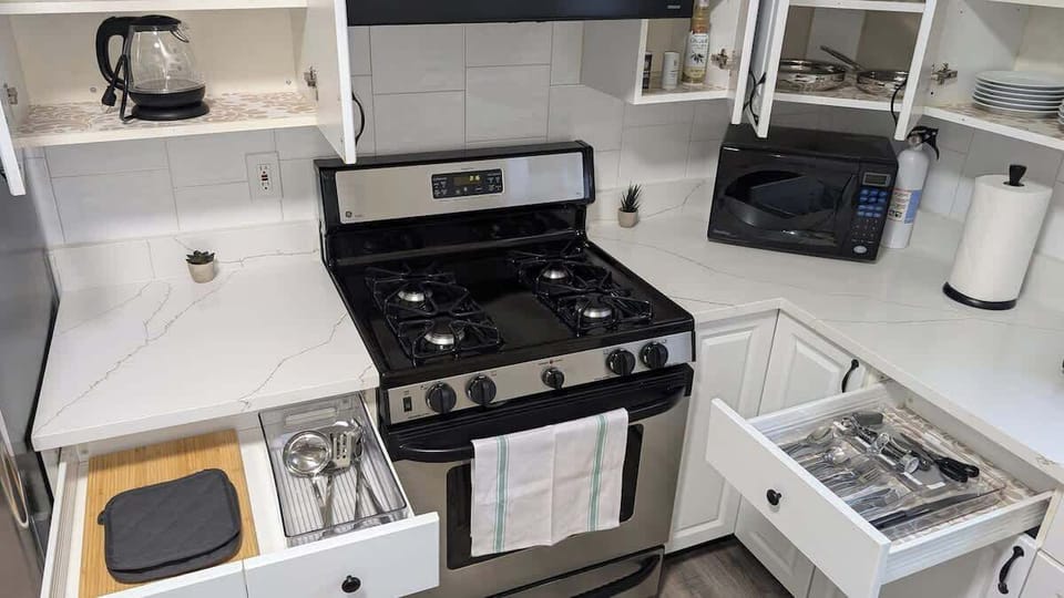 Fully equipped kitchen featuring modern appliances, including a gas stove, microwave, hot water kettle, and coffee maker, along with neatly organized drawers stocked with silverware and essentials—perfect for cooking your favorite meals
