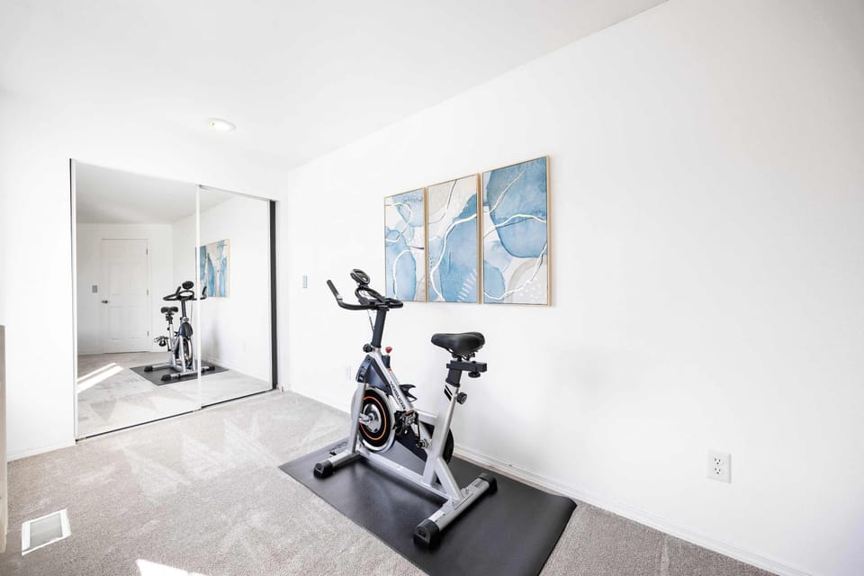 This room offers a dedicated exercise space equipped with a modern stationary bike, perfect for guests who like to stay active. The mirrored closet and wall art add to the room's refreshing, open ambiance.