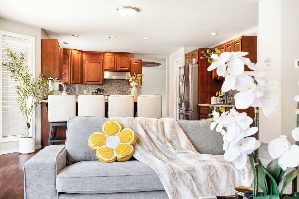 Another angle of the living room looking towards the kitchen, showing the seamless open-concept design. The sofa, decorative orchid on the coffee table, and bright space make this room perfect for lounging.