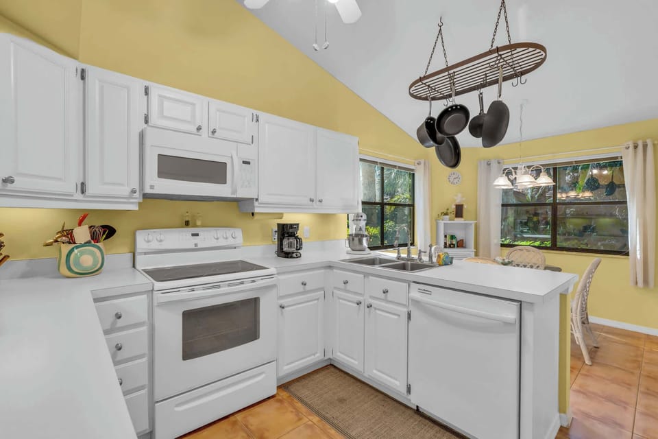 The kitchen has white appliances and cabinets and has direct lanai access (to the right) 