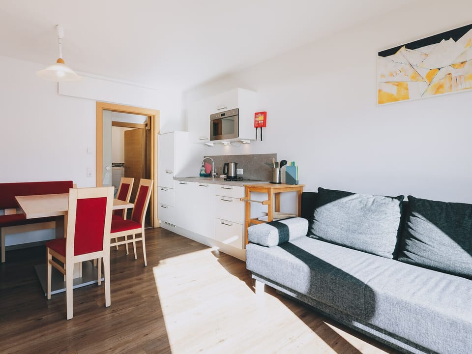 Dining room in the holiday apartment Apartments Haus Altenberger by we rent. Table with chairs and kitchen with stove, oven.