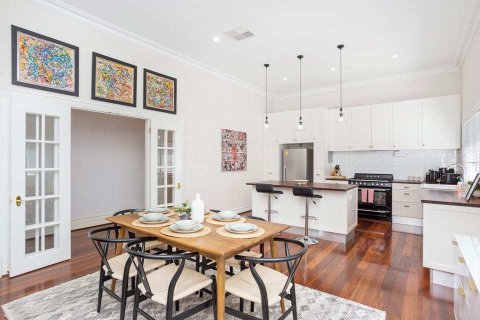 Enjoy meals in our spacious dining area, featuring a wooden dining table and chairs. Connected to the open-style kitchen with white cabinetry and a modern stovetop.
