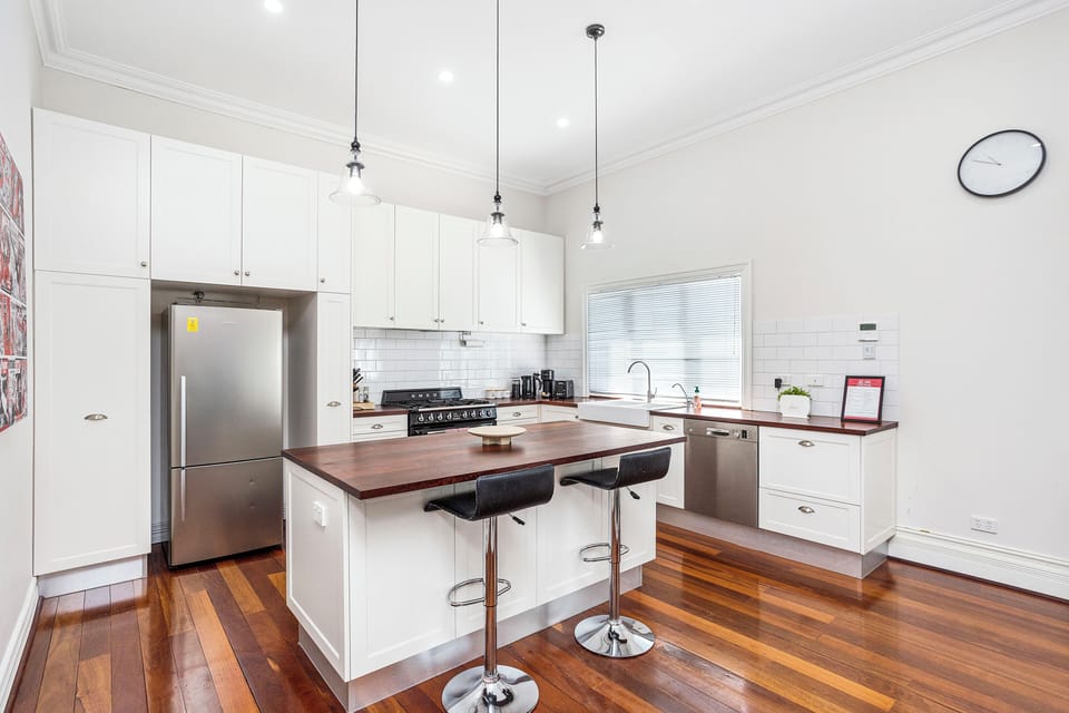 Discover a contemporary kitchen equipped with sleek white cabinets, a warm wooden countertop for a casual dining.