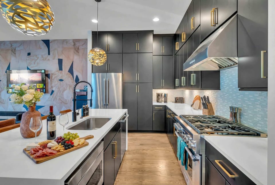 The kitchen island flows naturally from stove to sink to charcuterie spread, with overhead gold lighting turning meal prep into part of the gathering
