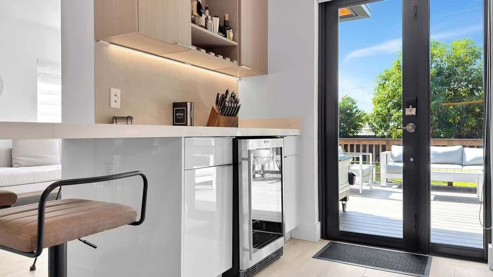Unwind in style. This modern home bar features a sleek quartz countertop, a built-in wine fridge, and a well-stocked bar cart, all opening up to a relaxing outdoor deck and patio.