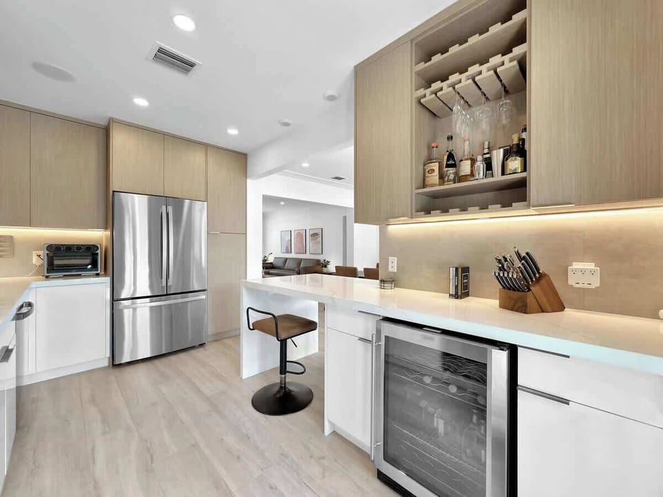 Unwind in this pristine modern kitchen and wet bar! Light wood cabinetry, sleek stainless appliances, and quartz counters create a stunning space. Grab a bottle from the built-in wine fridge and relax!