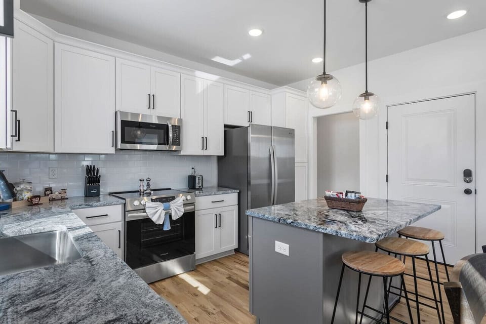 A modern, fully-equipped kitchen with a spacious island, perfect for meal prep and gatherings. Deep basin sink, ample counter space, and a sunny window view make cooking here a delight!