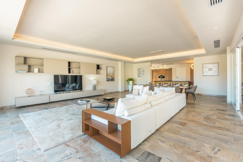 - Spacious living room with plush seating, warm lighting, and full entertainment setup for group stays  
- Natural tones and elegant décor enhance comfort throughout the space  
- Smooth indoor-outdoor connection offers serene views and fresh breezes