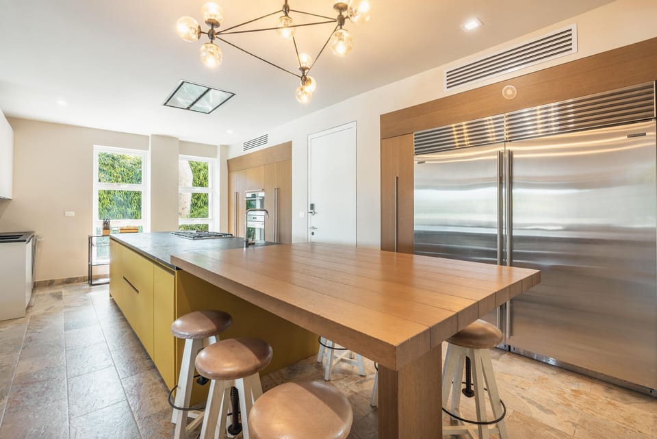- Modern kitchen featuring a large island, seating stools, and sleek stainless appliances for easy cooking  
- Bright windows bring in garden views for a fresh culinary experience  
- Spacious layout supports group dining and enjoyable vacation meal prep